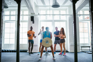 Fouten in krachttraining en afvallen: vrouw voert oefening uit terwijl ze wordt aangemoedigd door mede sporters.